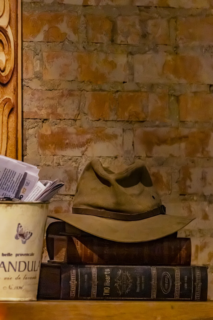Chapéu de feltro apoiado sobre livros antigos encadernados, contra parede de tijolo